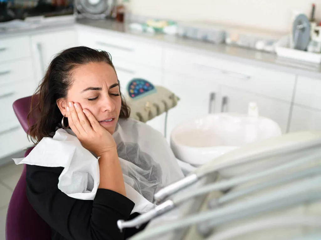 Patient in an exam chair holding the side of her face in pain.