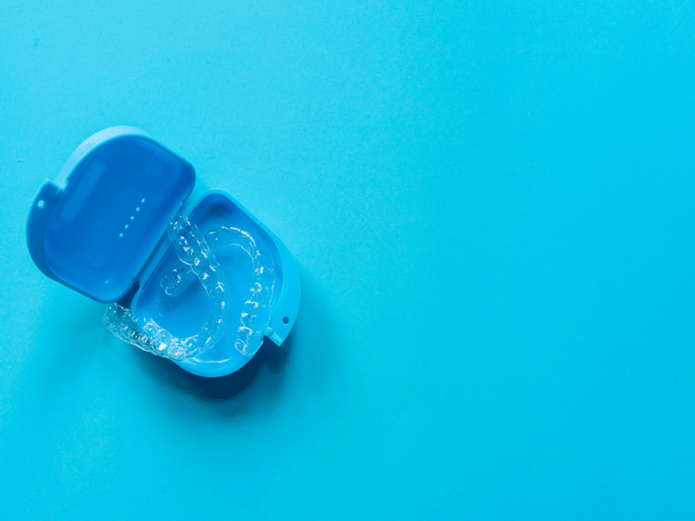 A blue Invisalign case on a blue background, holding a set of Invisalign clear aligners.