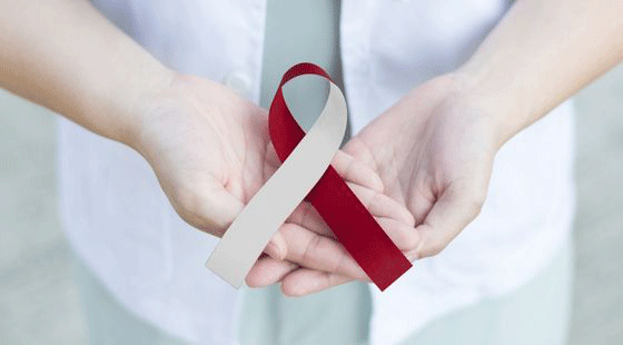 Hands holding a cream and red crossed ribbon, a symbol for oral cancer awareness.