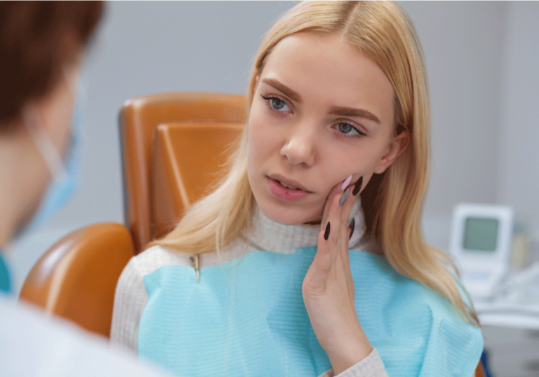 Young woman in a dental chair, holding her jaw in pain.