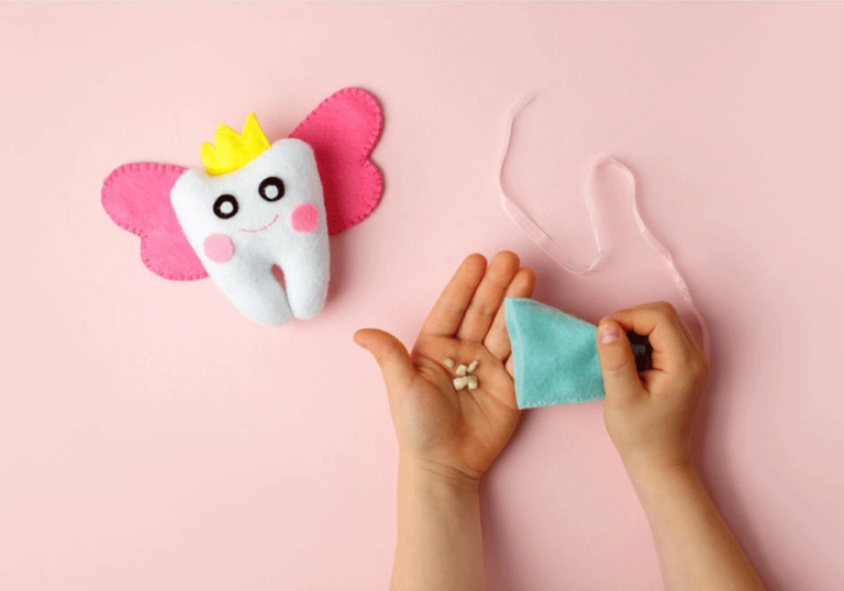 Child's hands holding baby teeth and a small blue bag, next to a plush tooth with pink wings and a crown.